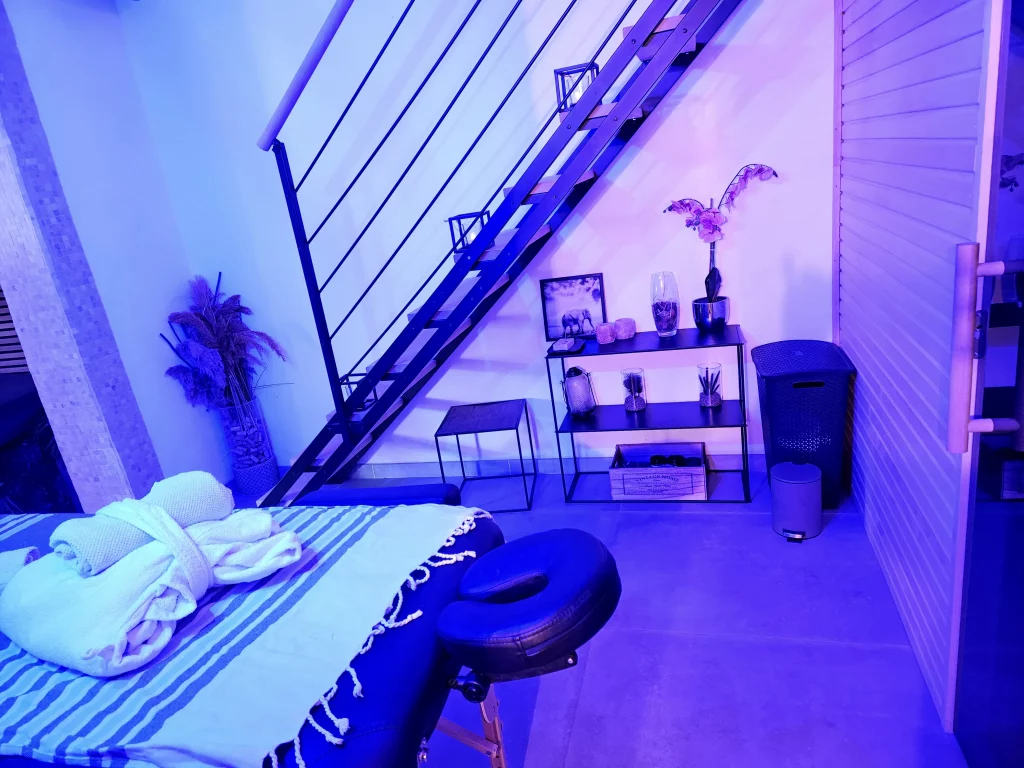 Espace de détente avec un lit de massage, éclairage bleu apaisant, sous un escalier moderne.