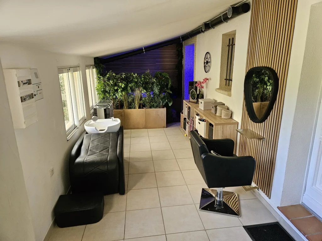 Salon de coiffure moderne à Auriol avec des sièges noirs, des plantes vertes et un éclairage bleu décoratif.