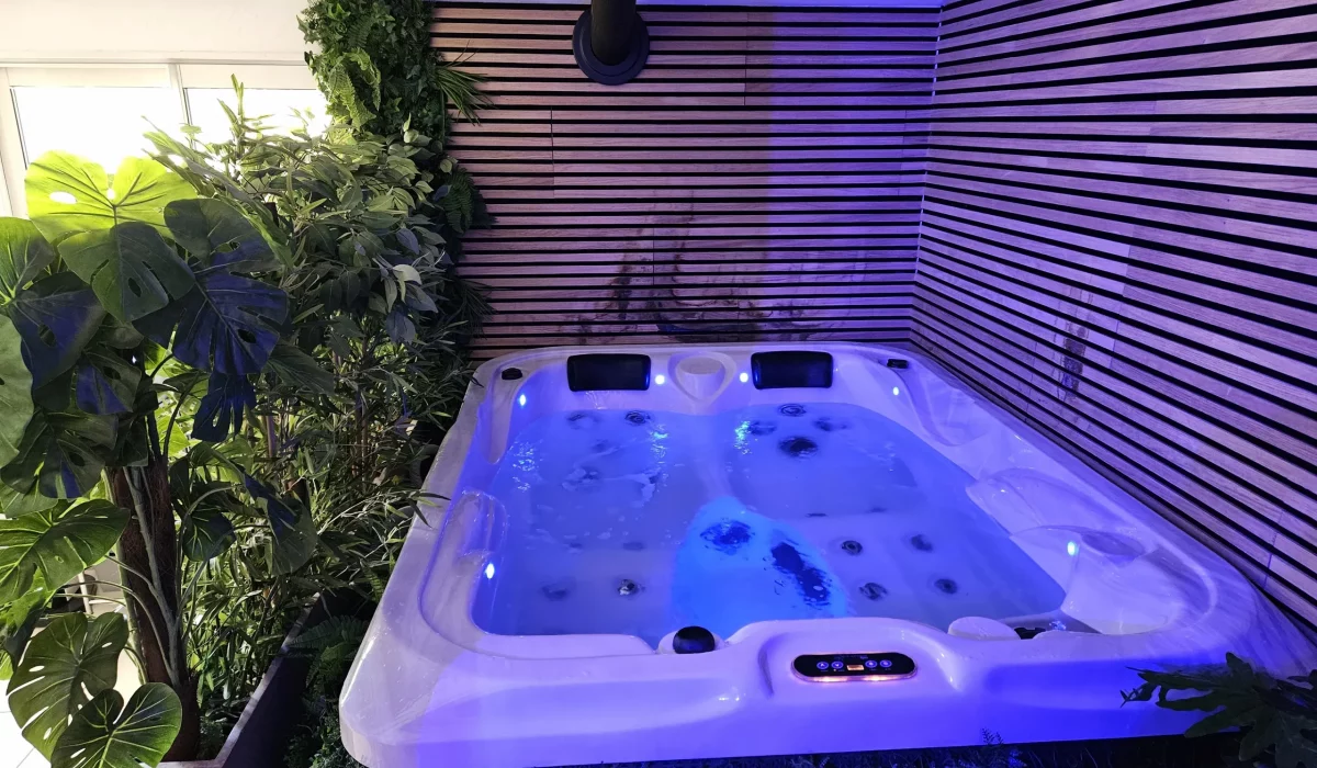 Jacuzzi avec éclairage bleu et végétation luxuriante dans un espace intérieur moderne.